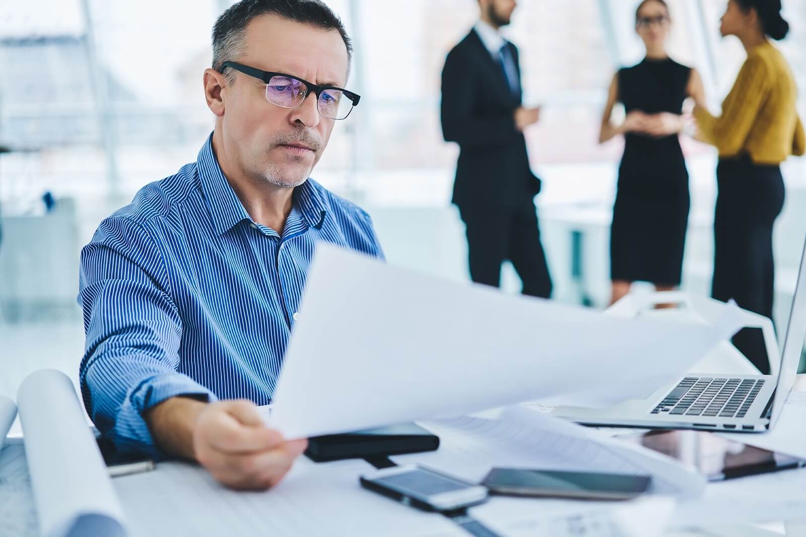 Man in blue collared shirt looking at papers while sitting at his desk.