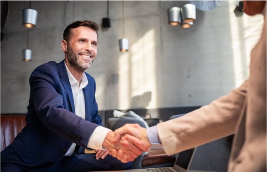 Man in a sports coat shaking another mans hand.