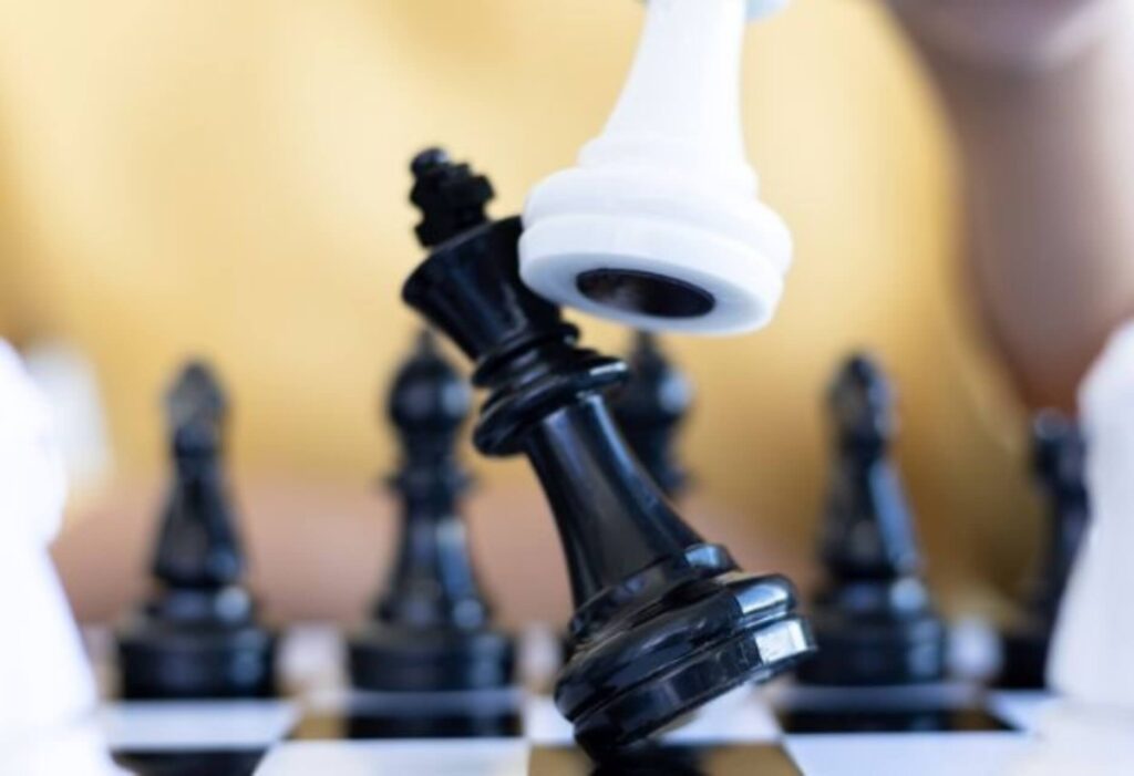 A white chess piece being used to knock over a black one